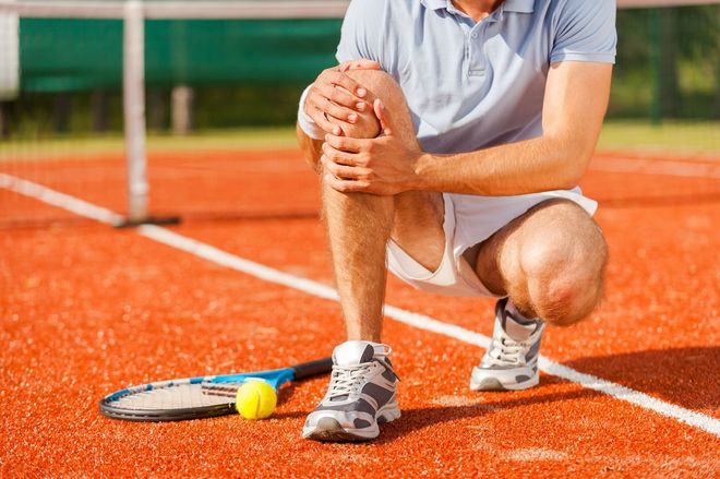 Tennis player crouching on clay court with racket and ball near the baseline