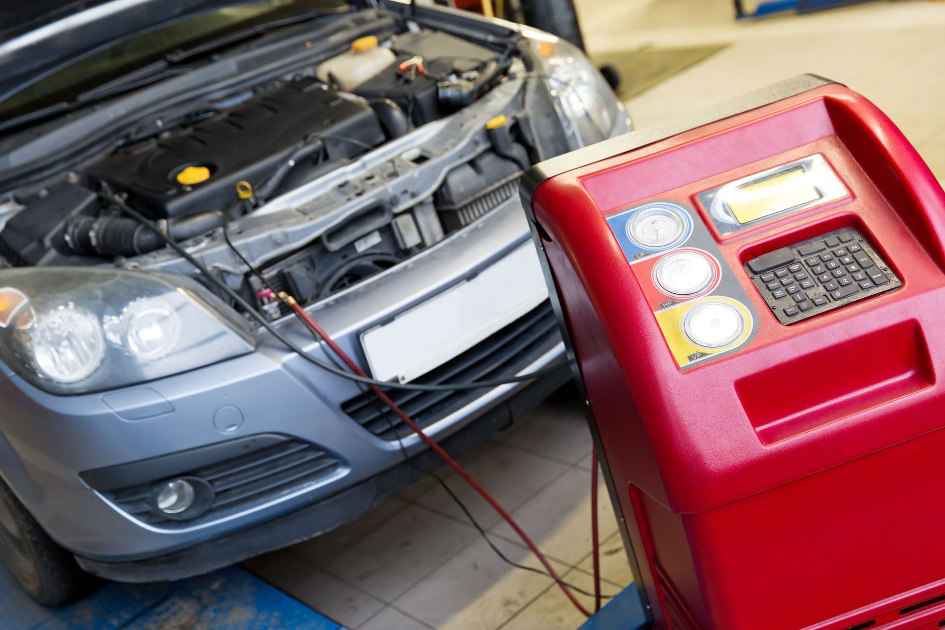 Car being serviced, connected to red AC recharge machine in a garage.