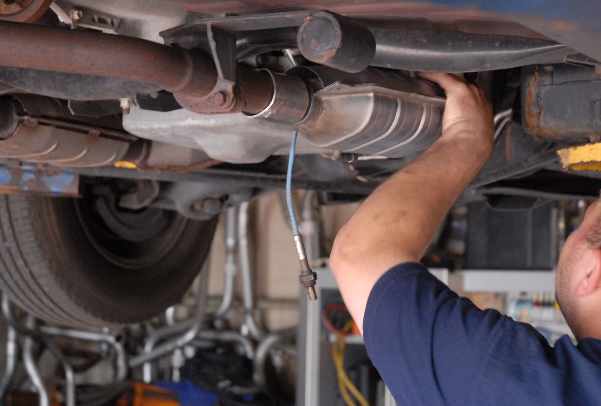 Mechanic working on the underside of a car, examining exhaust system components.
