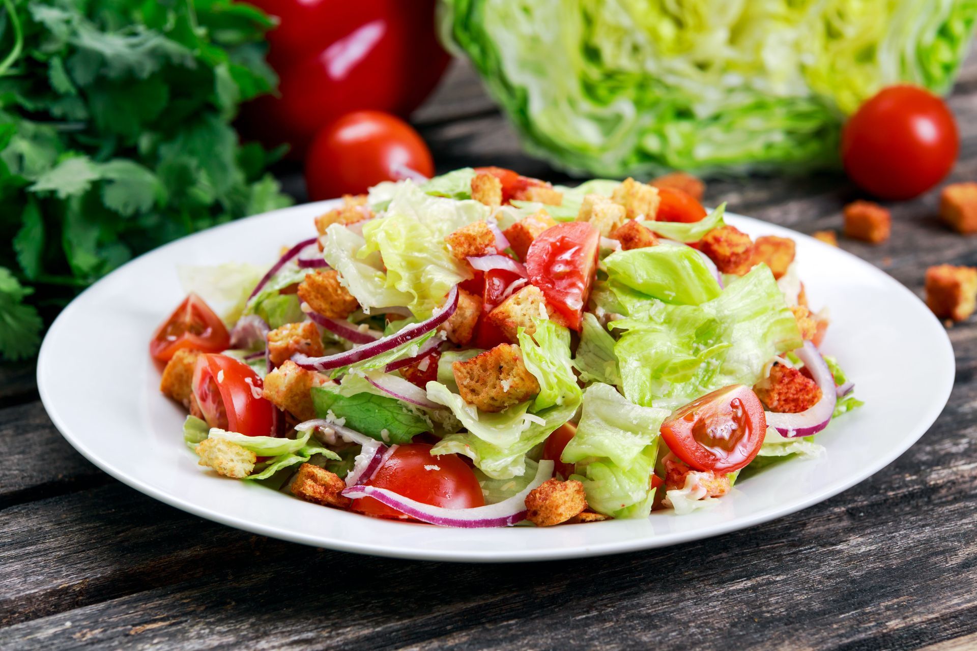 A plate full of salad in front of a head of lettuce and some tomatoes.