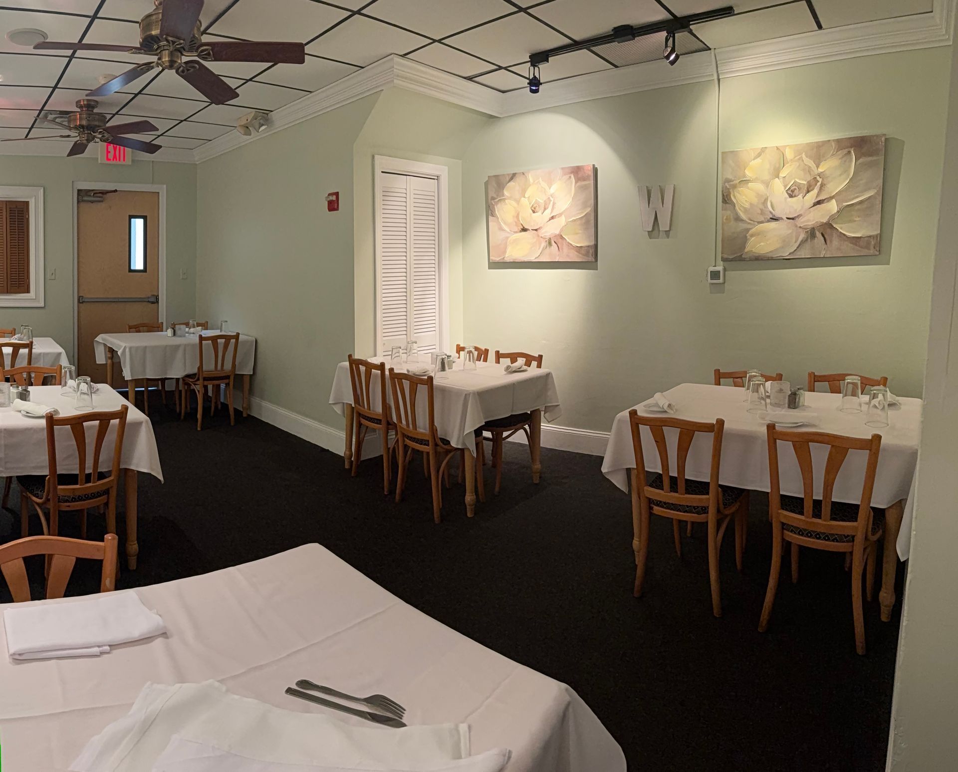 Quiet dining room with white tablecloths, wooden chairs, wall art, and ceiling fans.