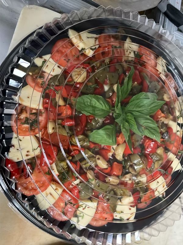 A plastic container filled with tomatoes, peppers, cheese, and basil