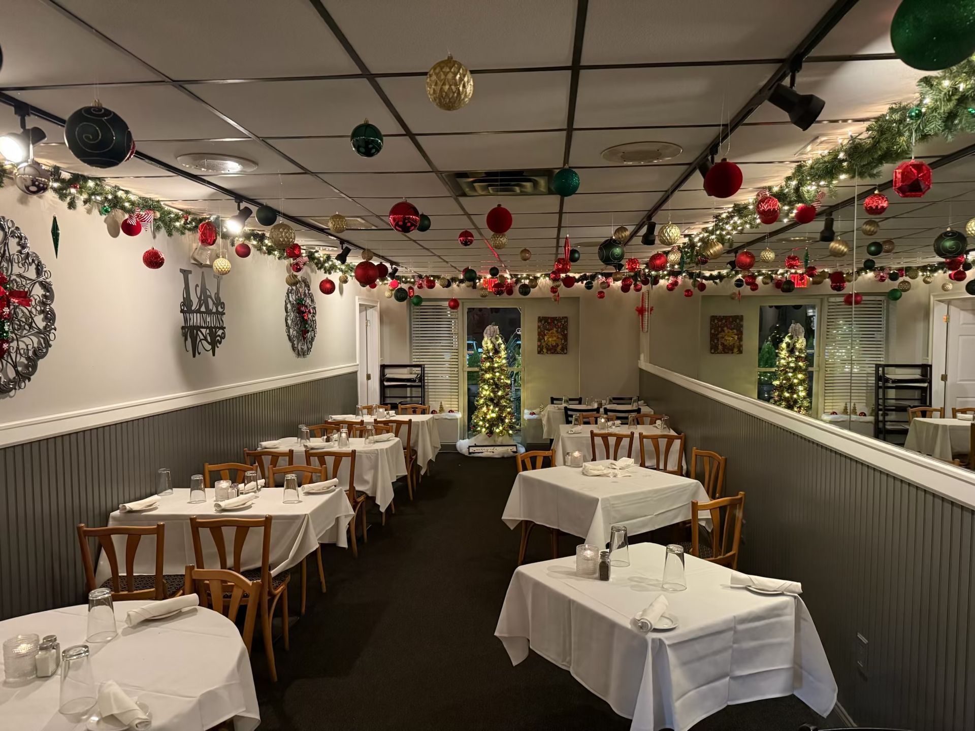 Restaurant interior decorated for Christmas, with tables set for dining. Ornaments and garland hang from the ceiling.