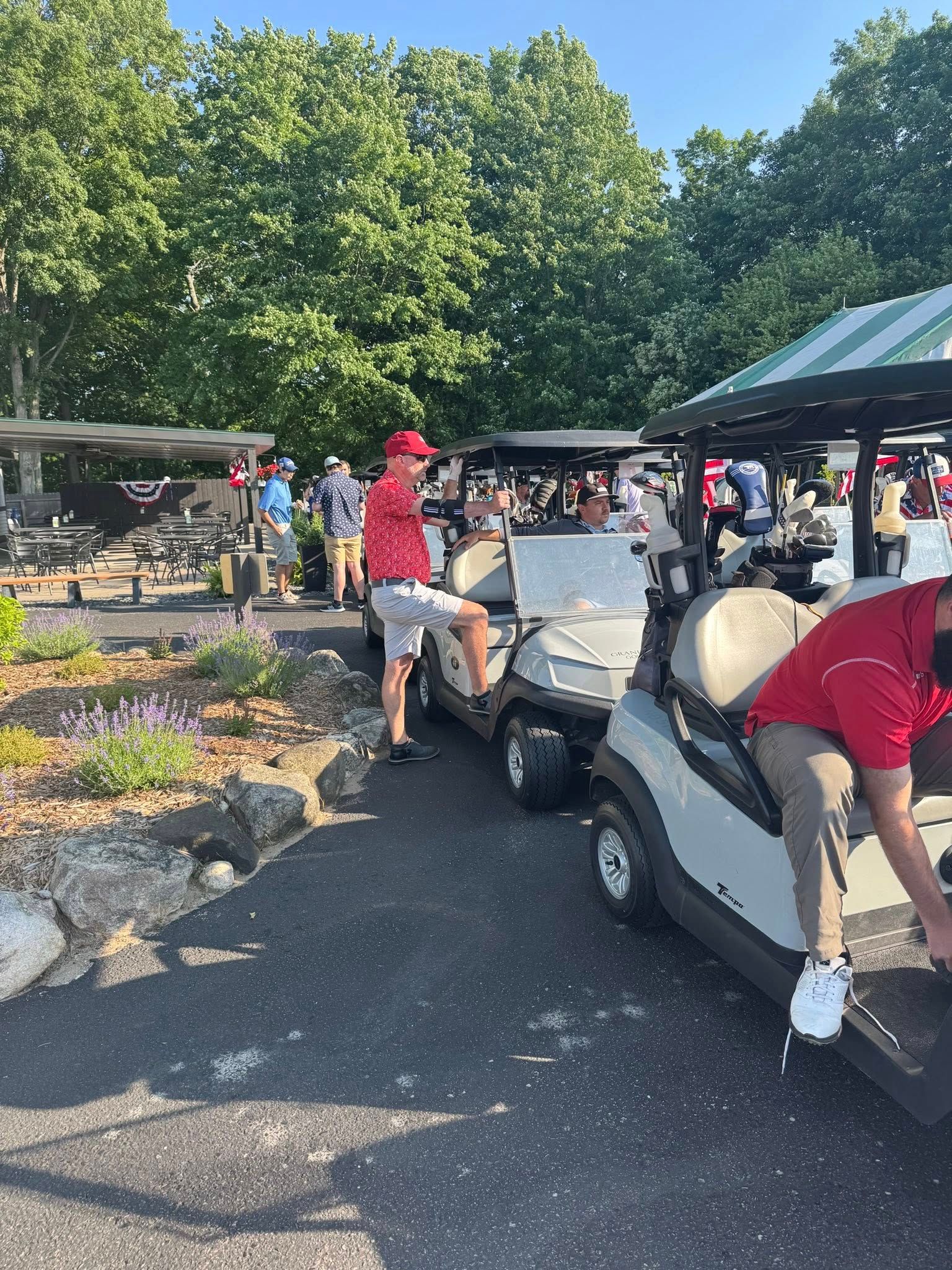 People in golf attire near golf carts at a golf course. Some are standing, and others are in the carts.