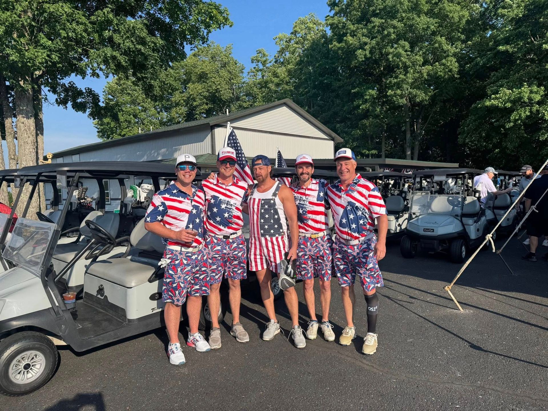 Five men in matching American flag outfits stand in front of golf carts on a sunny day.