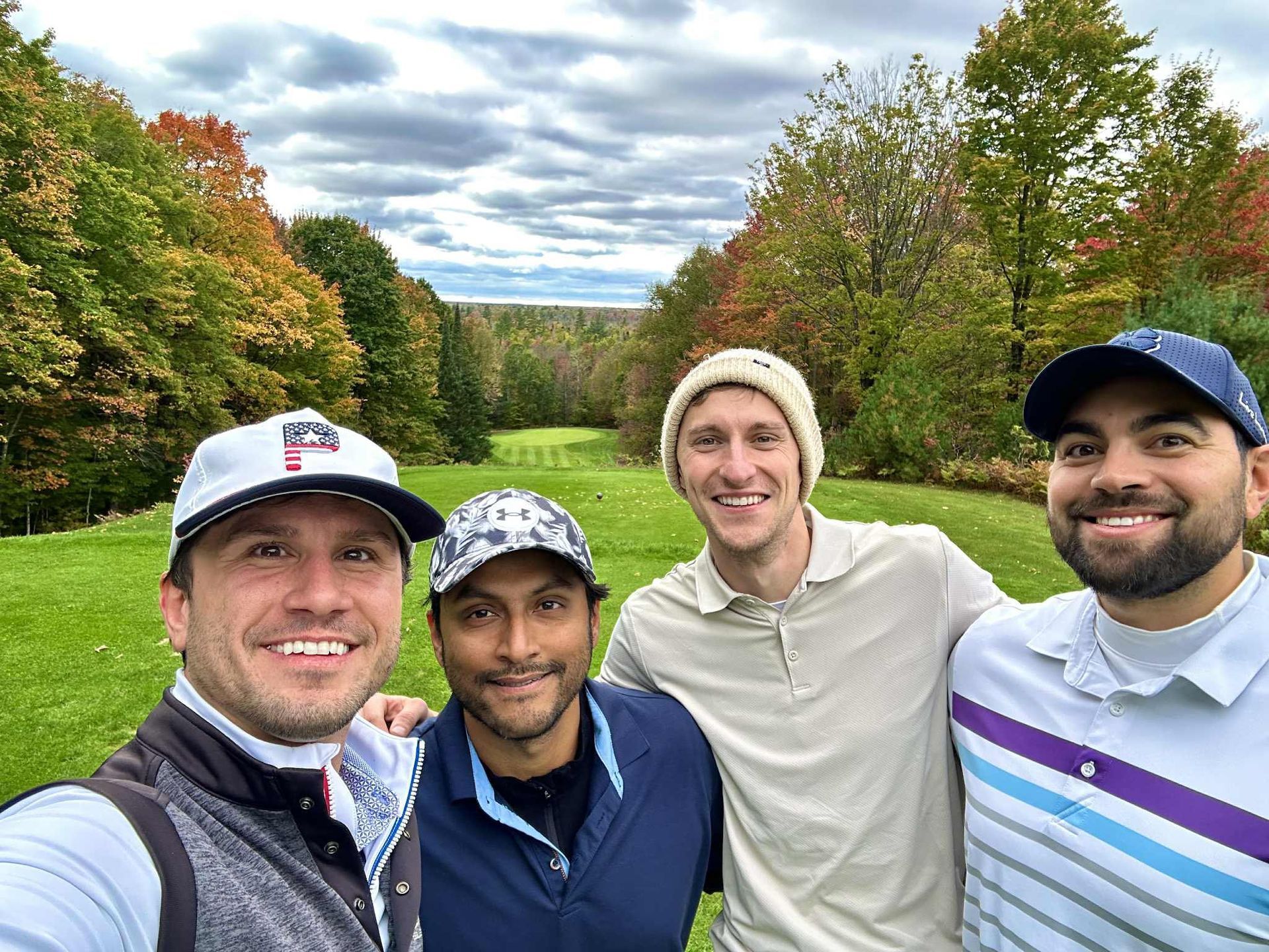 Four men pose for a selfie on a golf course with fall foliage.