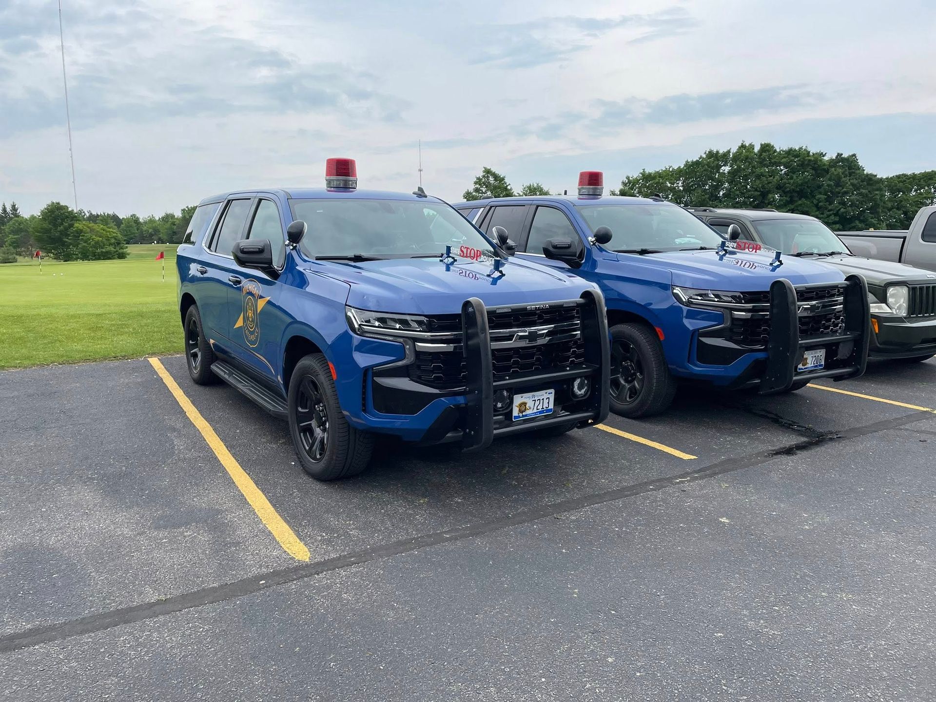 Two blue police SUVs parked in a lot, each with red lights and push bars.