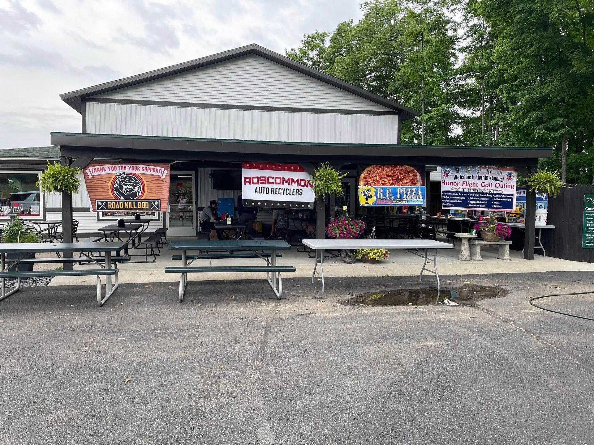 Restaurant with outdoor seating. Banners advertise food specials. Gray building with picnic tables.
