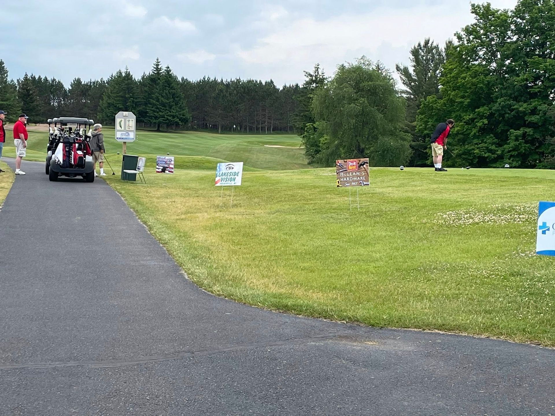 Golfer teeing off on a green golf course, a golf cart nearby.