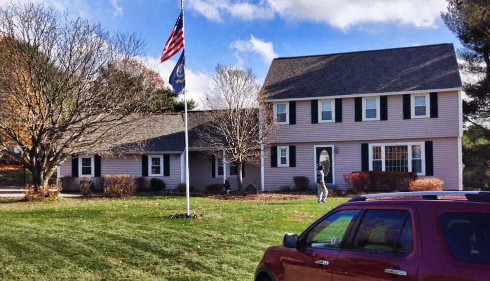 A red truck is parked in front of a house with an american flag flying in the background.