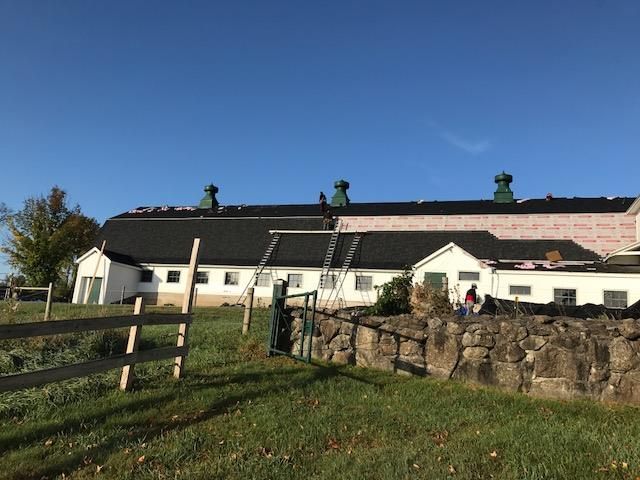 A large white house with a black roof is sitting in a grassy field next to a stone wall.