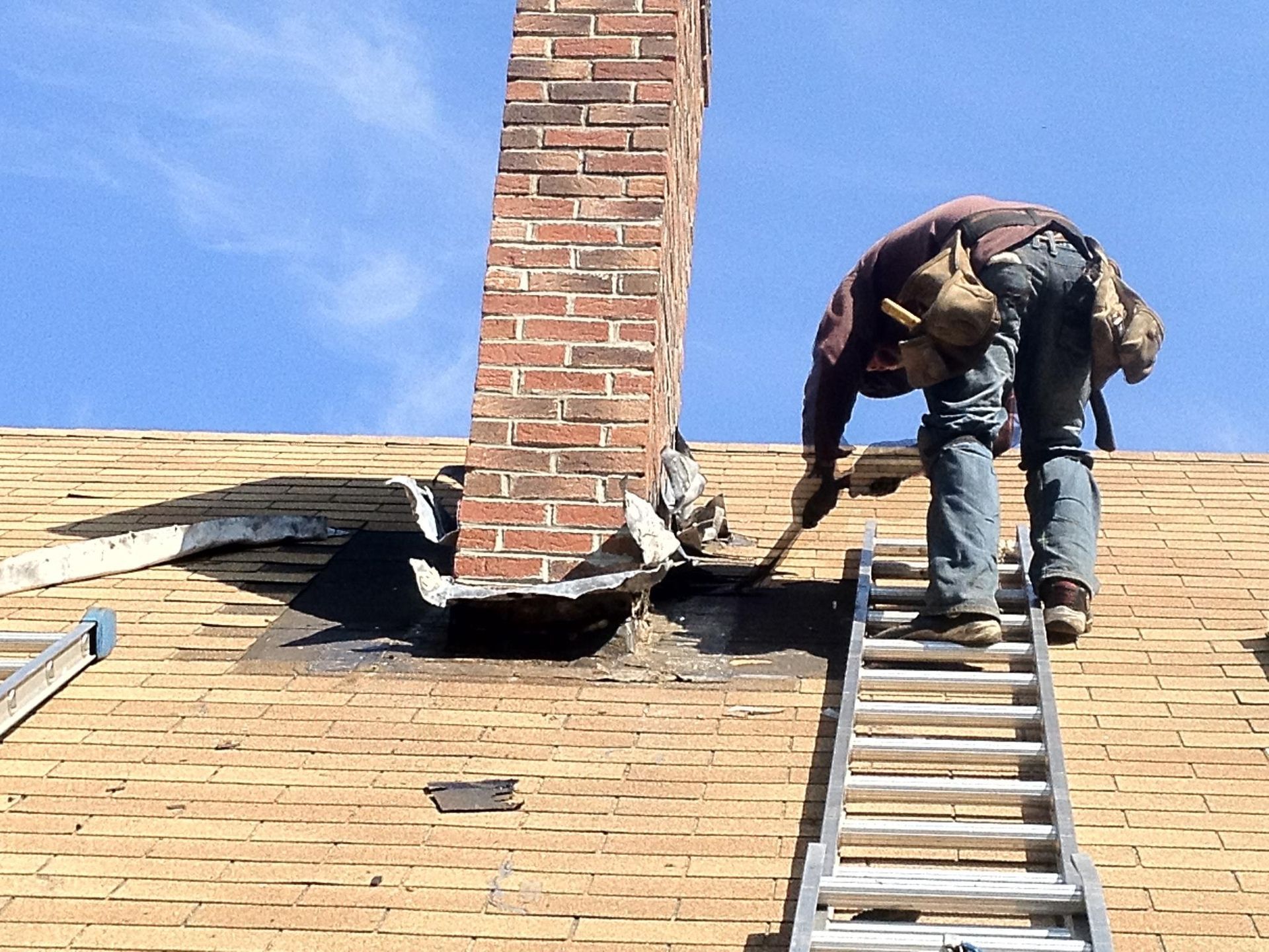 A man on a ladder is working on a roof next to a chimney