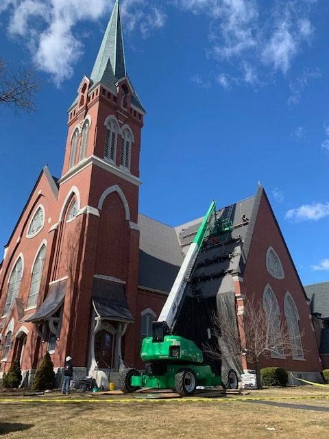 A green crane is sitting in front of a large red brick church.