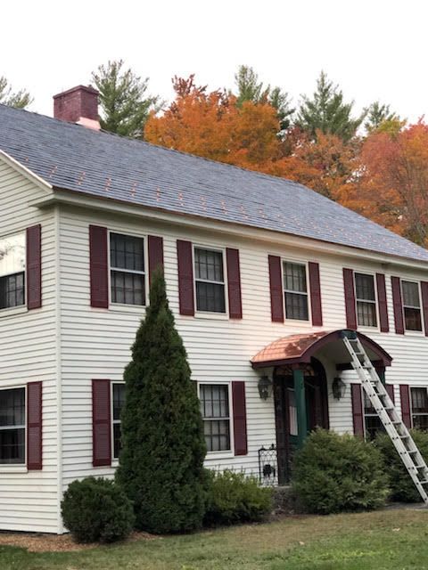 A large white house with red shutters and a ladder in front of it.