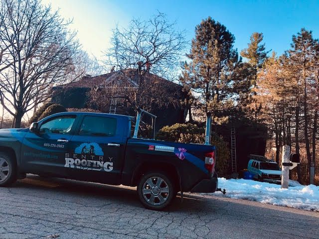 A blue roofing truck is parked in front of a house.