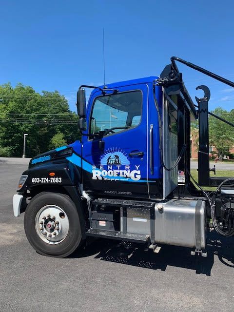 A blue roofing truck is parked in a parking lot
