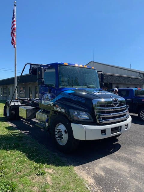 A dump truck is parked in front of a building with an american flag in the background.