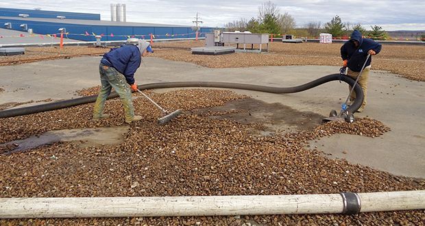 Two men are cleaning the roof of a building with a vacuum cleaner.