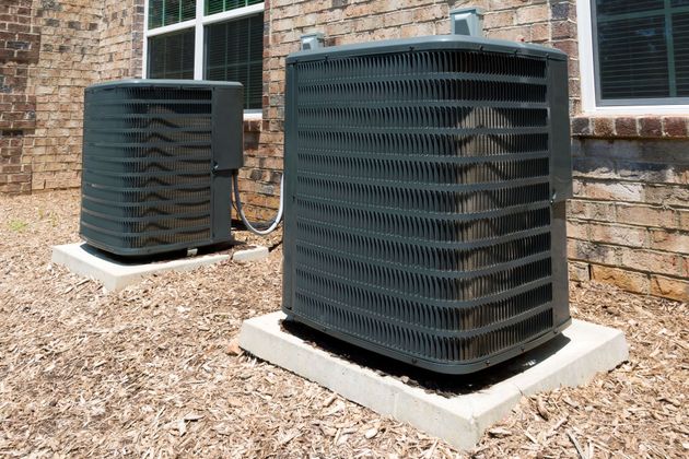 Two black outdoor HVAC units on concrete pads beside a brick building.