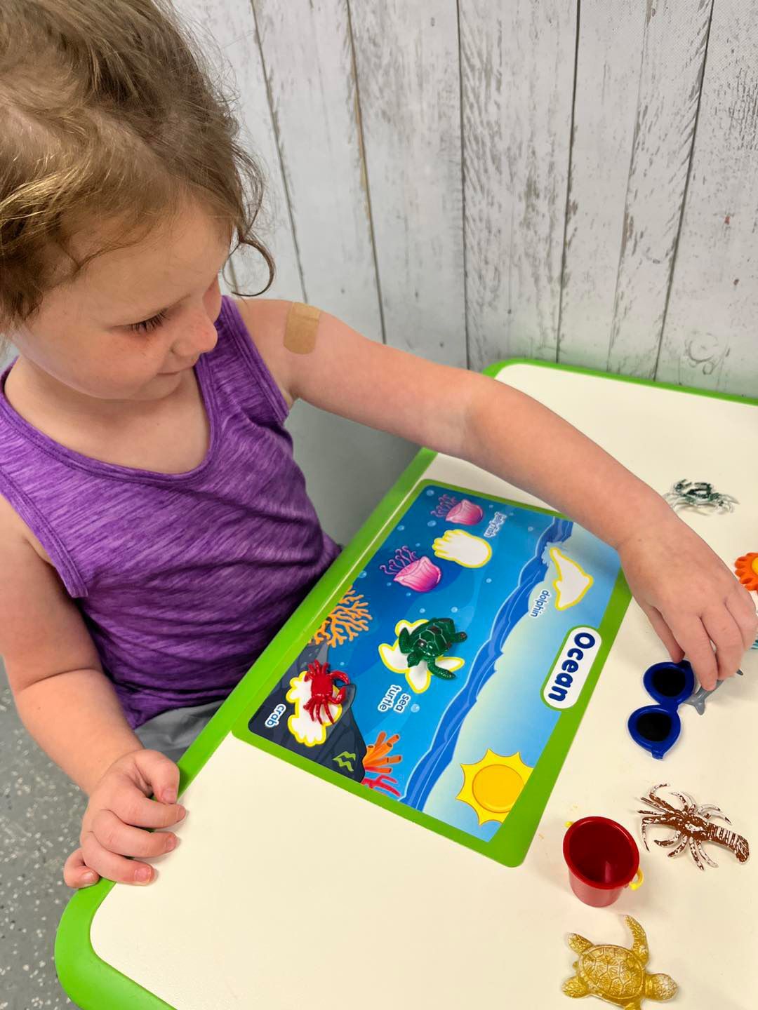 A little girl is sitting at a table playing with toys.