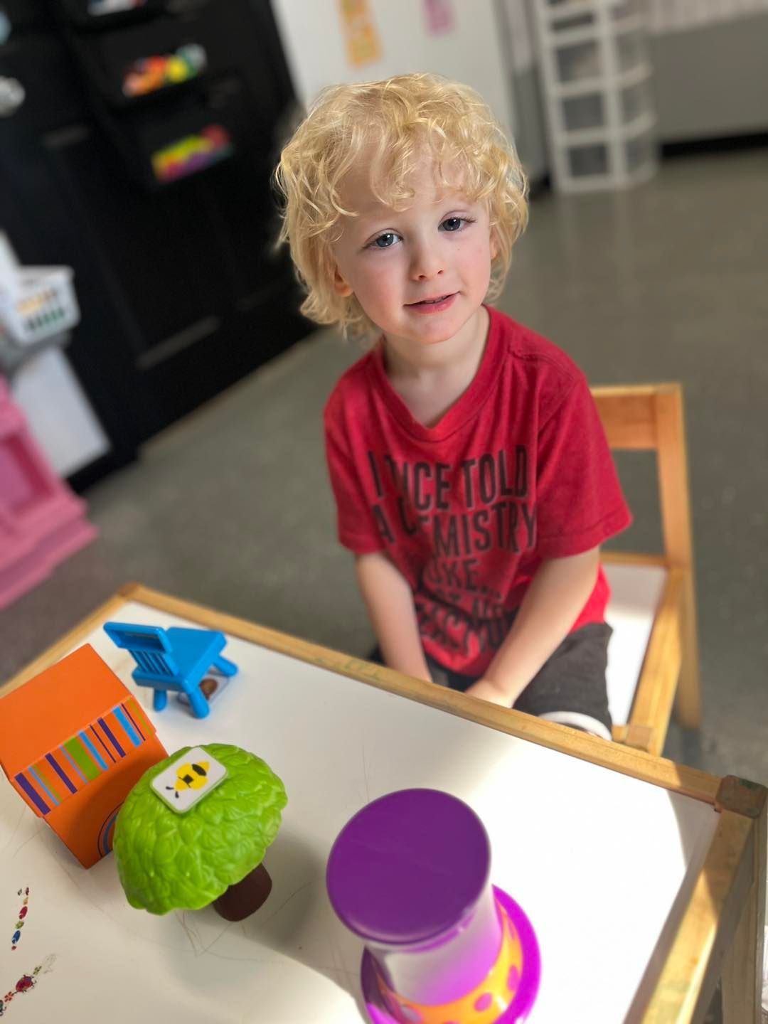 A young boy in a red shirt is sitting at a table with toys