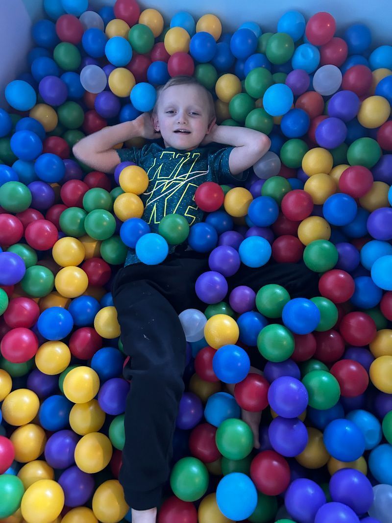 A young boy is laying in a ball pit filled with colorful plastic balls.