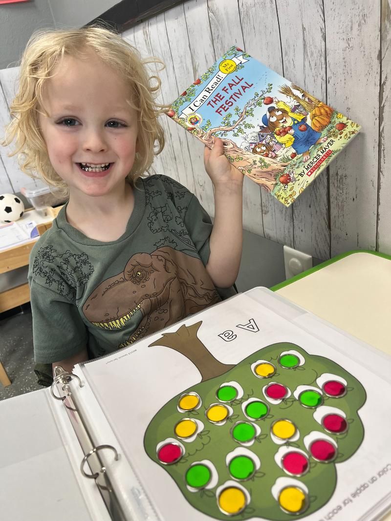 A young boy is sitting at a table holding a book.