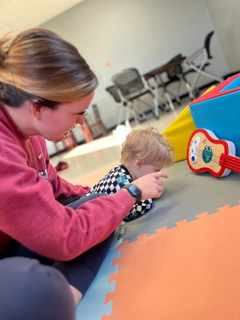 A woman is playing with a baby on the floor next to a guitar.