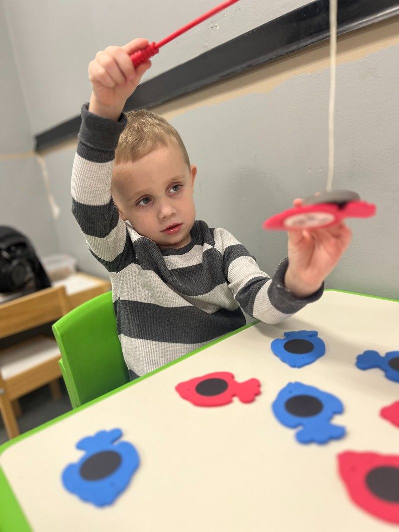 A young boy is sitting at a table playing with a fishing rod.