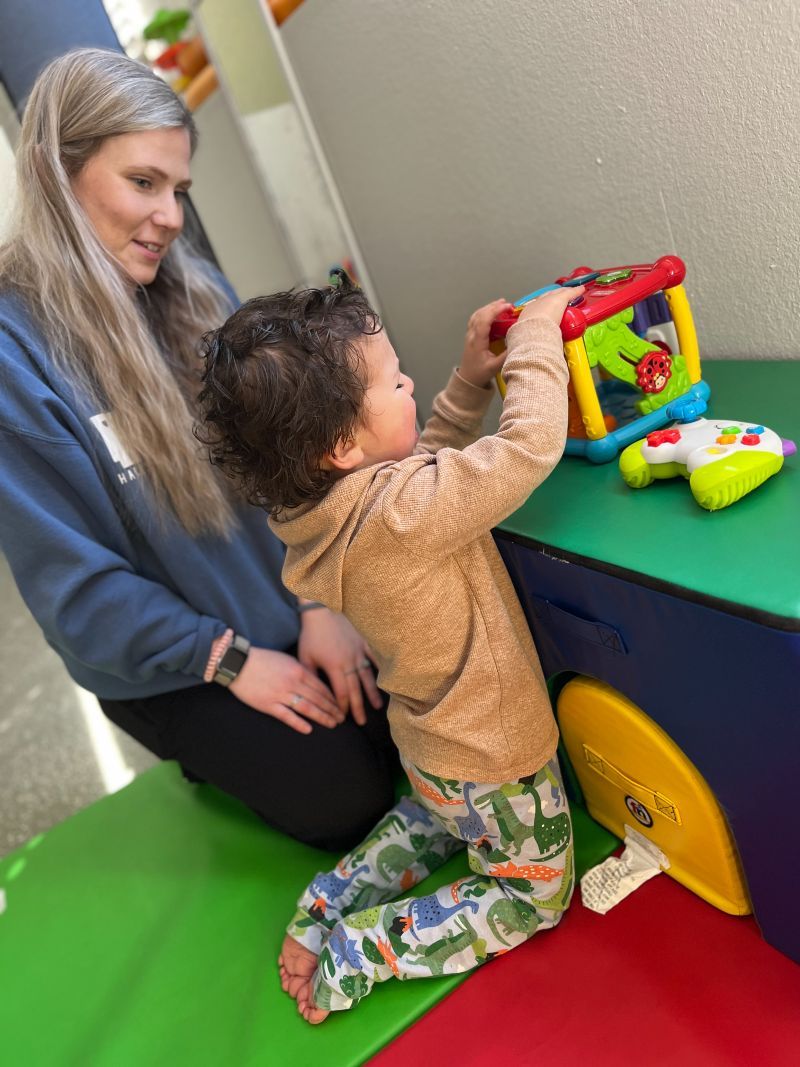 A woman is kneeling down next to a child playing with a toy.