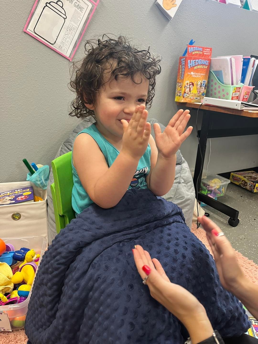 A little girl is clapping her hands while sitting on a blue blanket.