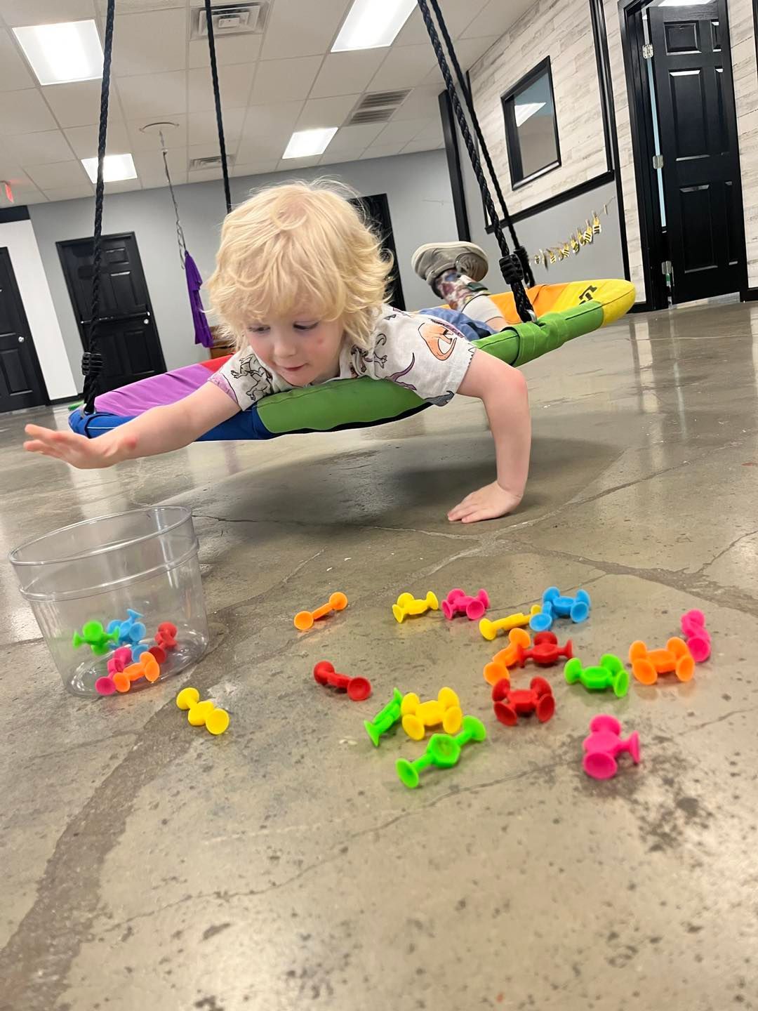 A little boy is doing push ups on a swing in a room.