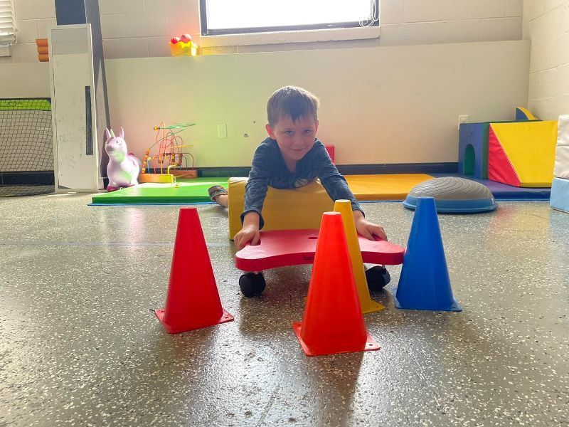 A young boy is playing with a scooter and cones on the floor.