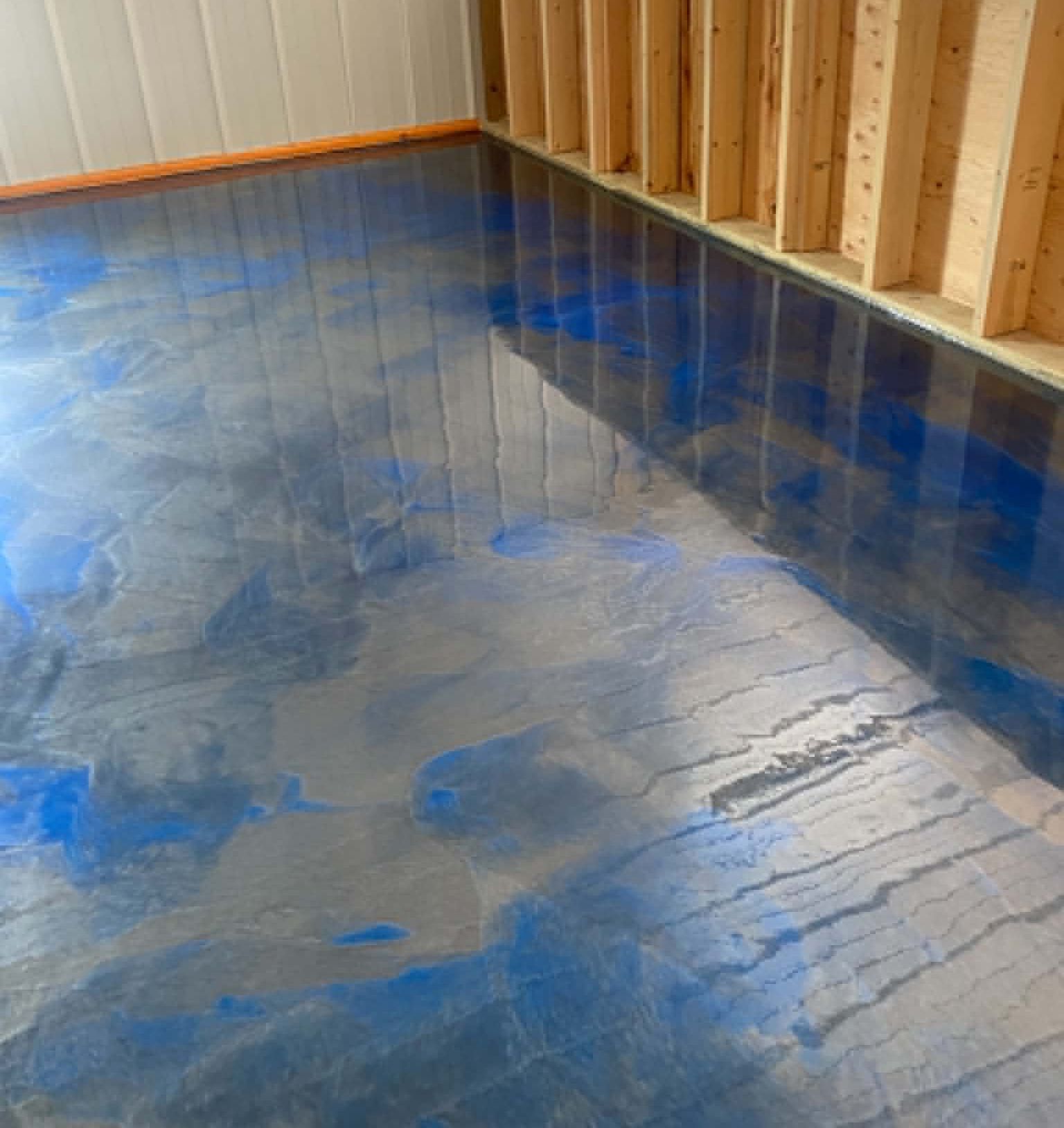 Blue epoxy floor in a partially framed room with wood stud walls and baseboards.