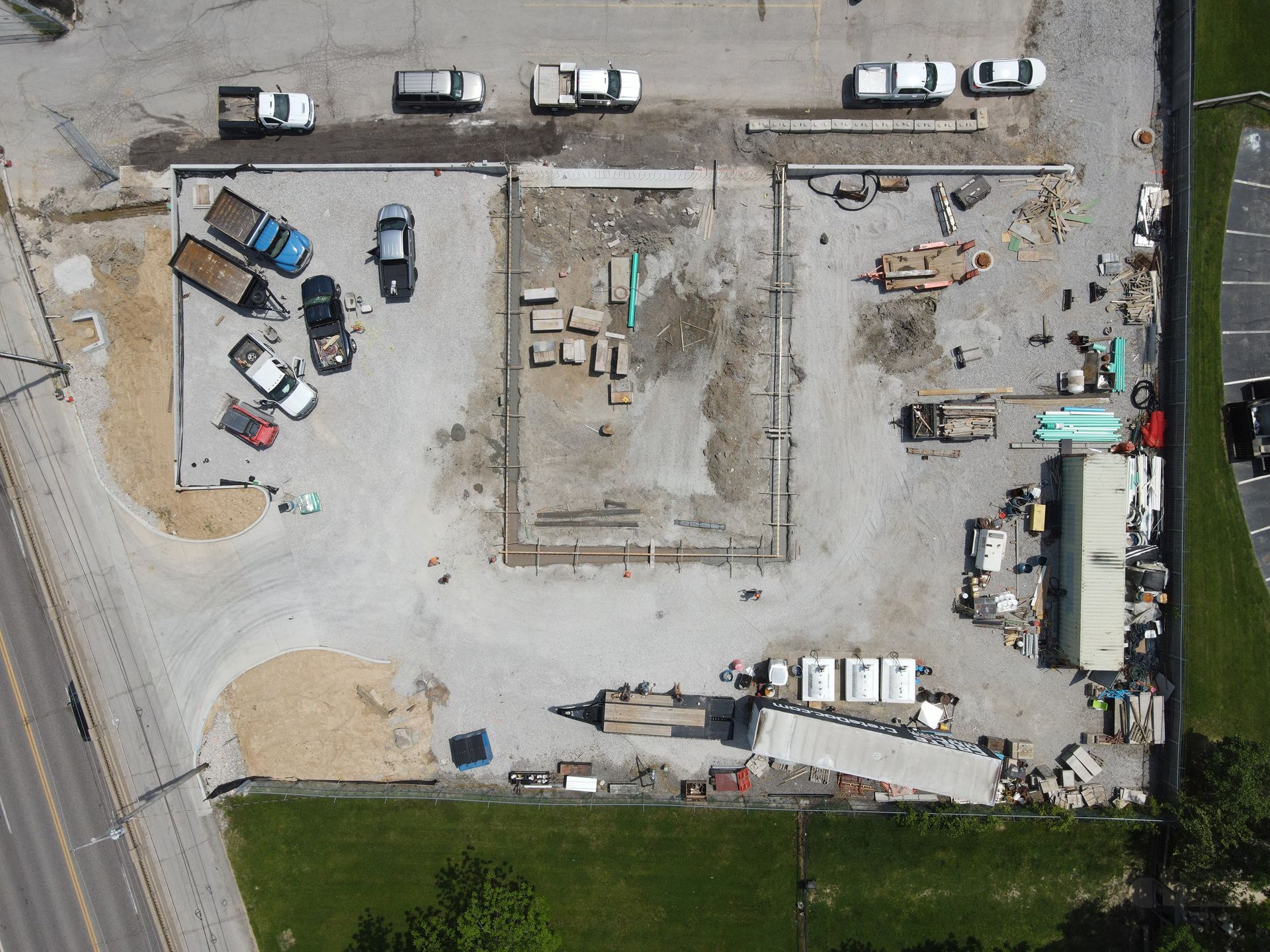 Aerial view of a construction site with concrete foundation, parked vehicles, and building materials.