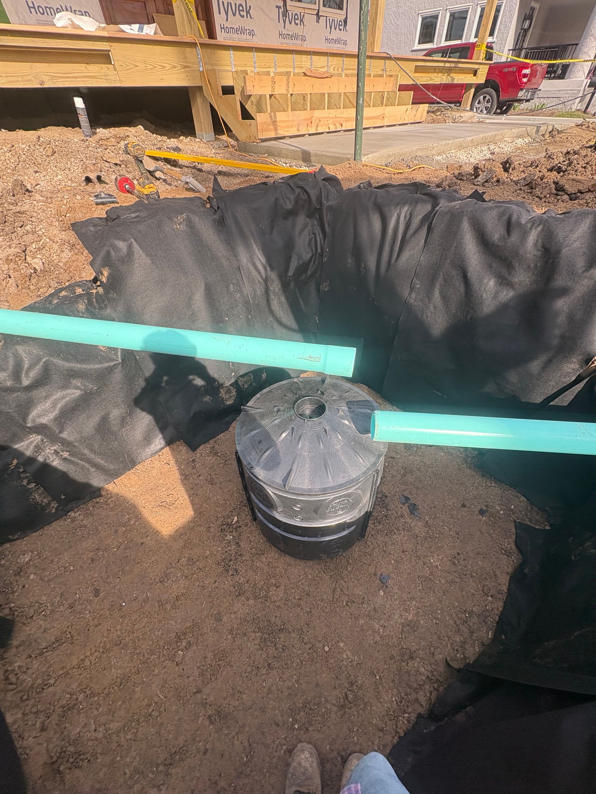 Construction site with black waterproof liner and a metal bucket in a dug-out area under repair.