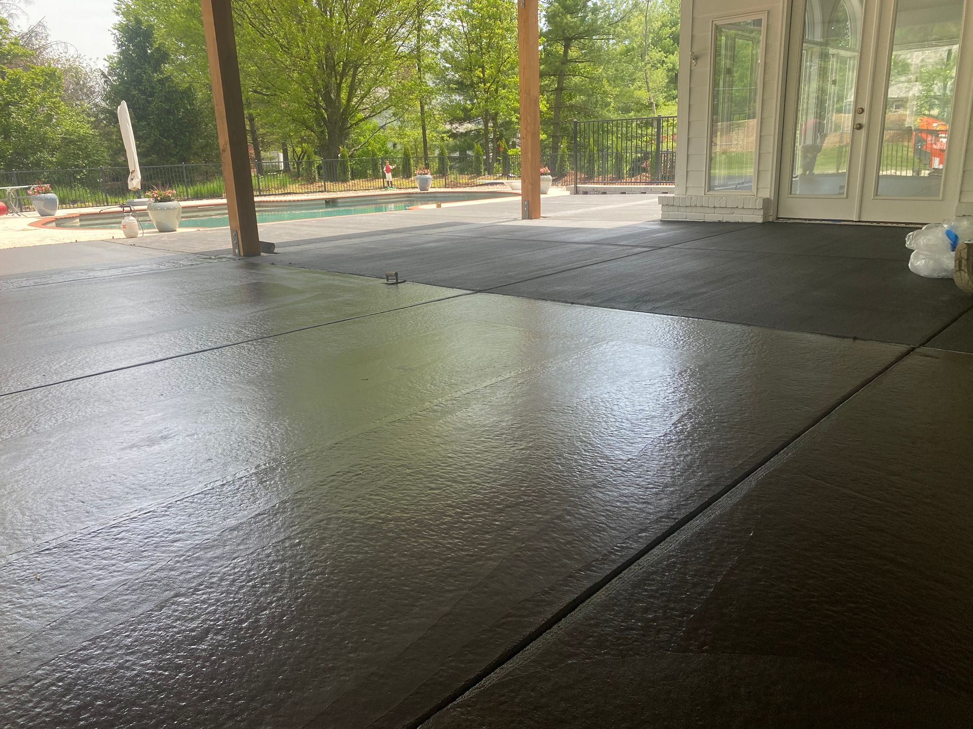 Wet concrete patio under a covered area, with trees and glass doors in the background.
