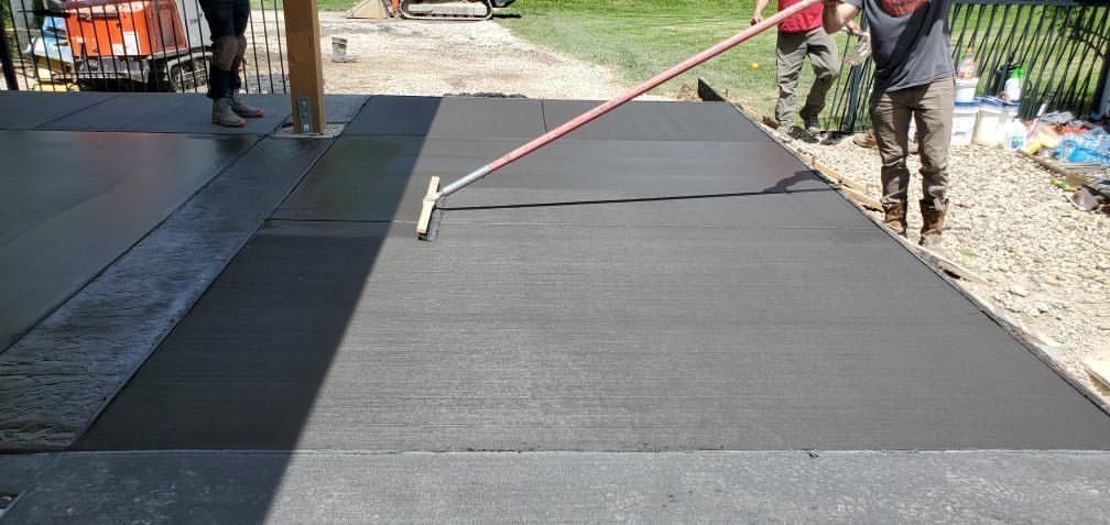 Workers smoothing fresh black pavement with a long-handled squeegee outdoors.