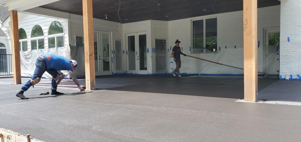 Workers painting a covered porch exterior, with one kneeling and one using a roller on the wall.