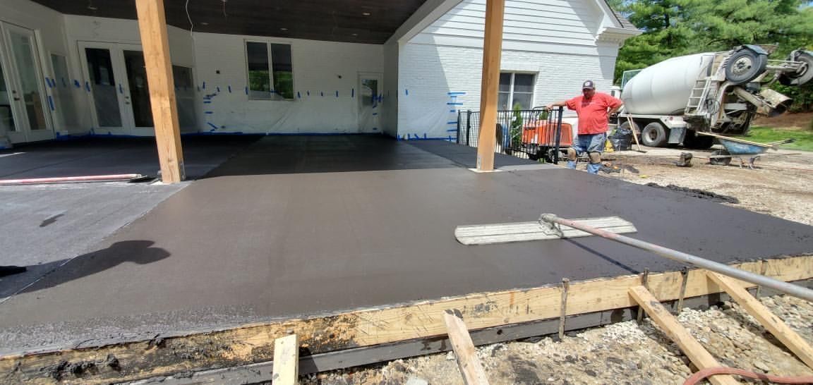 Fresh black asphalt being paved in a residential driveway with workers and a cement mixer nearby.