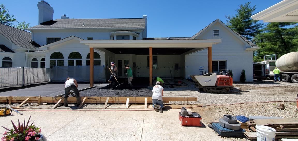 Workers pouring a concrete patio in front of a white house with a covered porch.