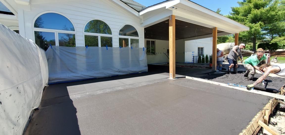House exterior with white arches, covered patio, and workers paving a driveway.