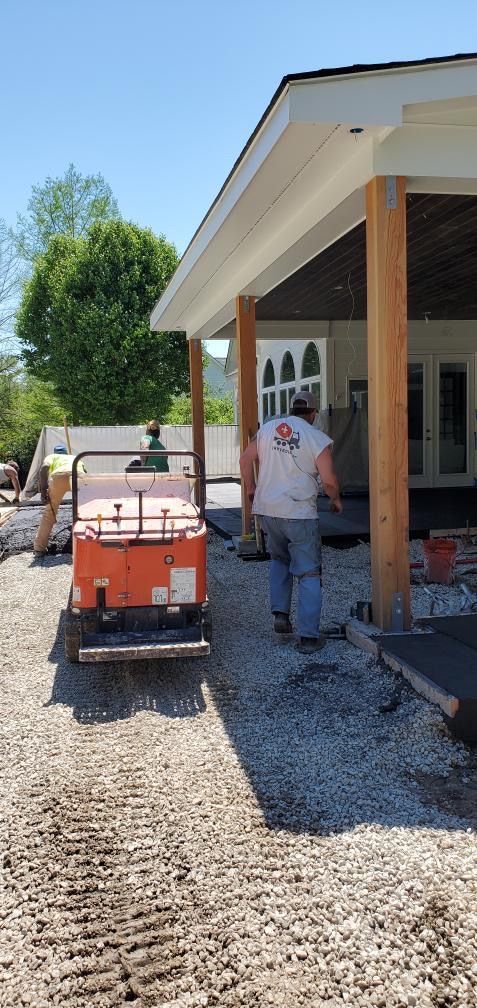 Worker spreading gravel beside a house with a skid steer on a gravel driveway.