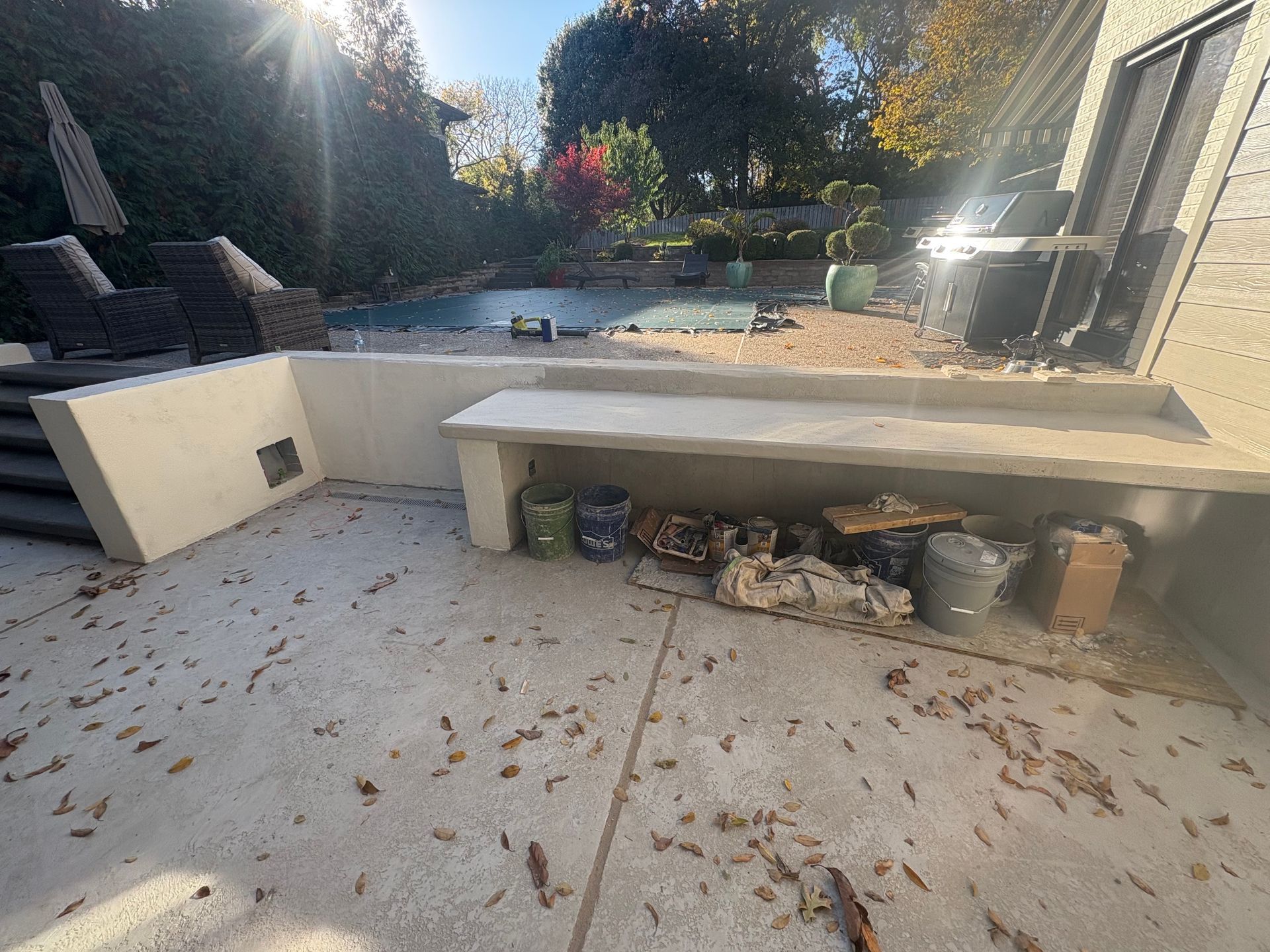 Outdoor patio with built-in concrete bench, potted plants, and sunlit garden in the background.