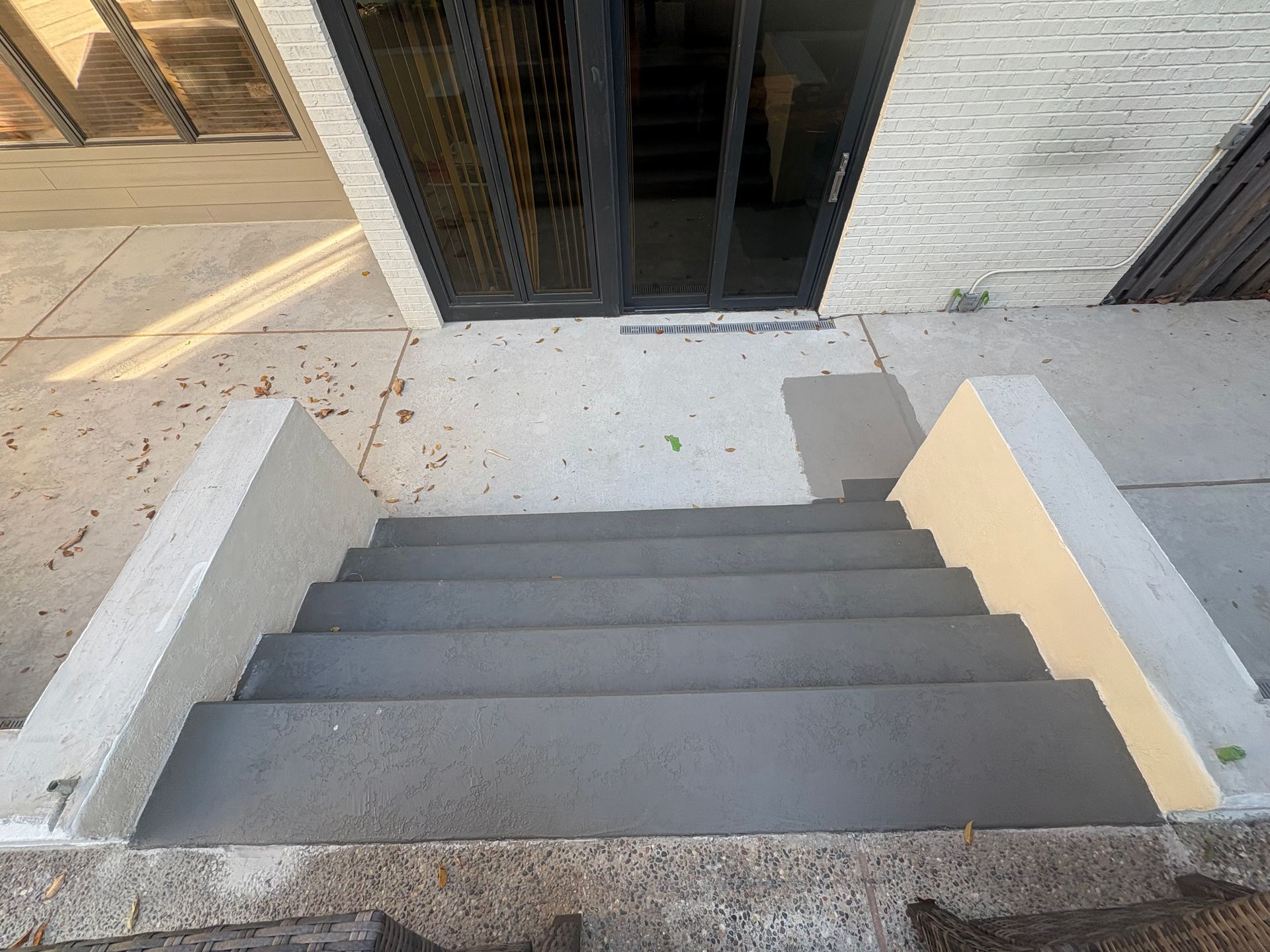 Concrete steps leading to a dark glass doorway with white walls on either side.