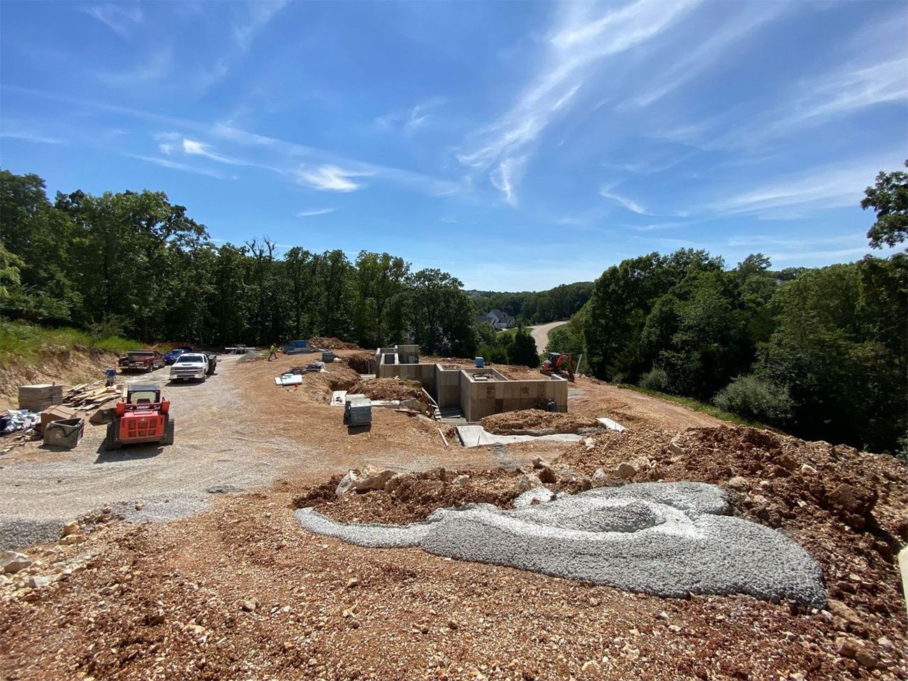 Construction site with excavators, gravel piles, and dirt under a blue sky with trees in the background.