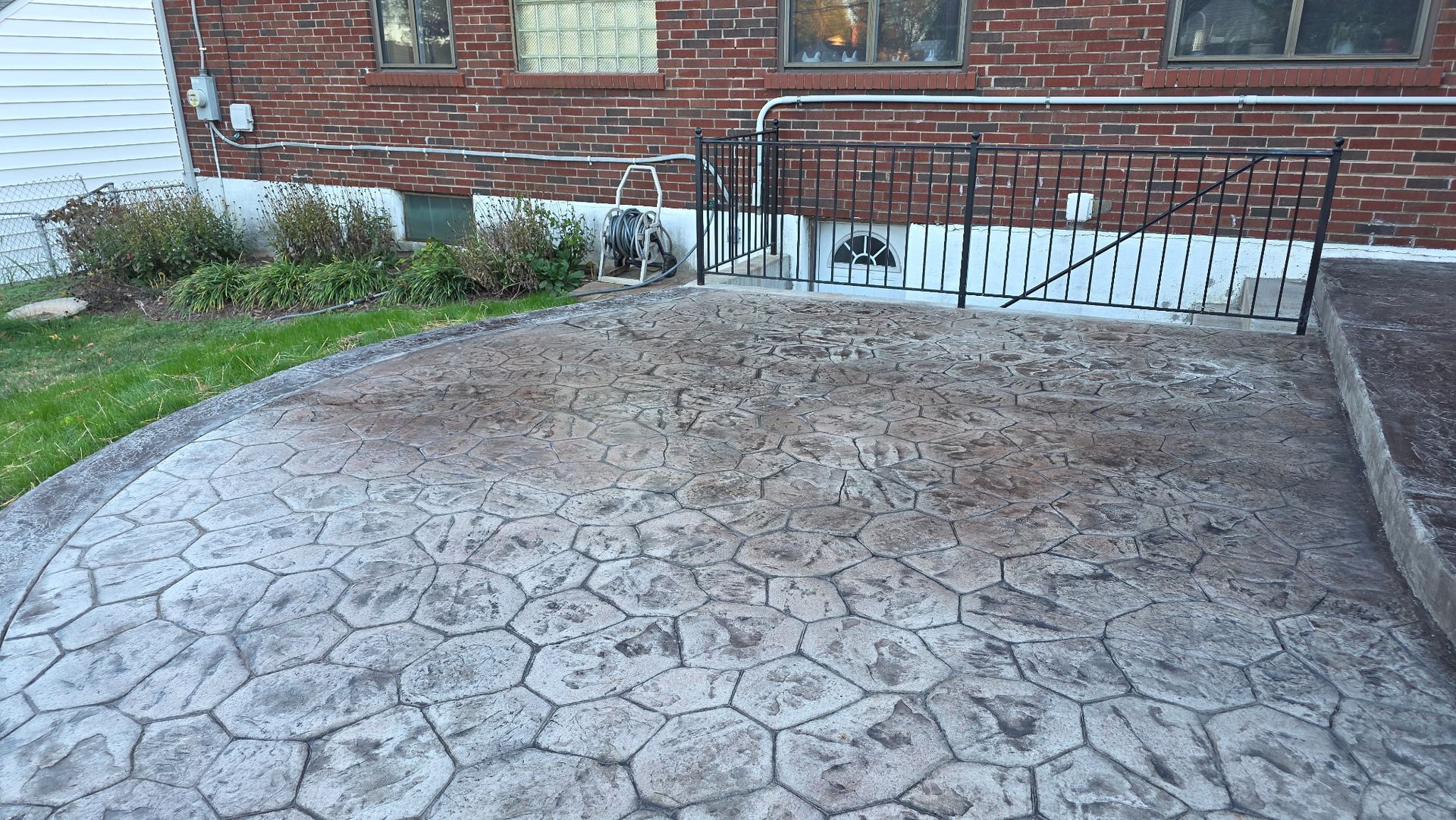 Cracked concrete driveway leading to a red-brick house with a black metal railing and small shrubs.