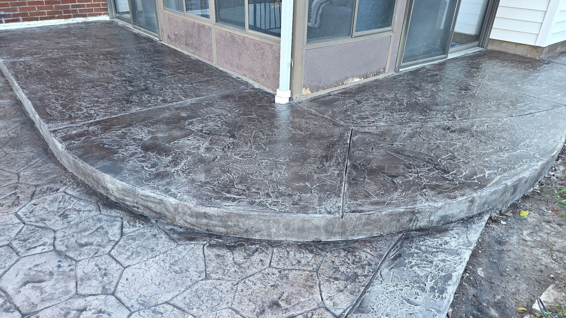 Corner of a building with a curved concrete sidewalk and wet ground after rain.