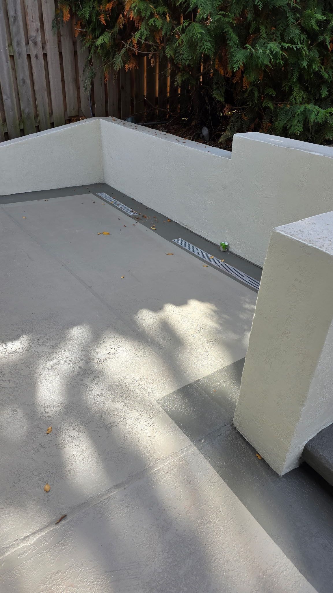 Small outdoor patio with white walls, concrete floor, and sunlight/shadow from nearby trees.