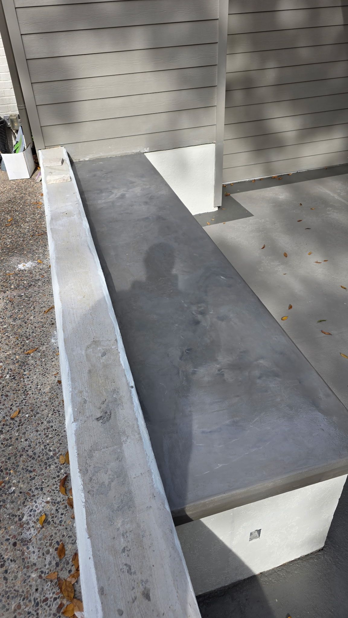 Concrete bench against a wall in an outdoor shaded area.